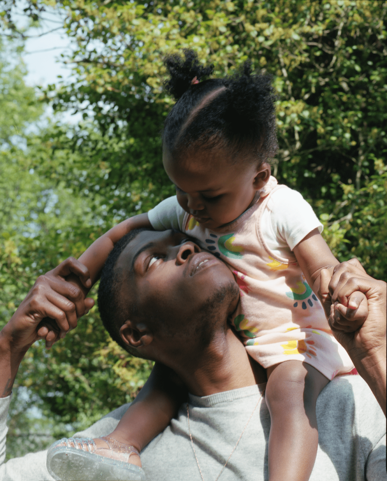 A young father carries his baby daughter on his shoulders, looking up at her.