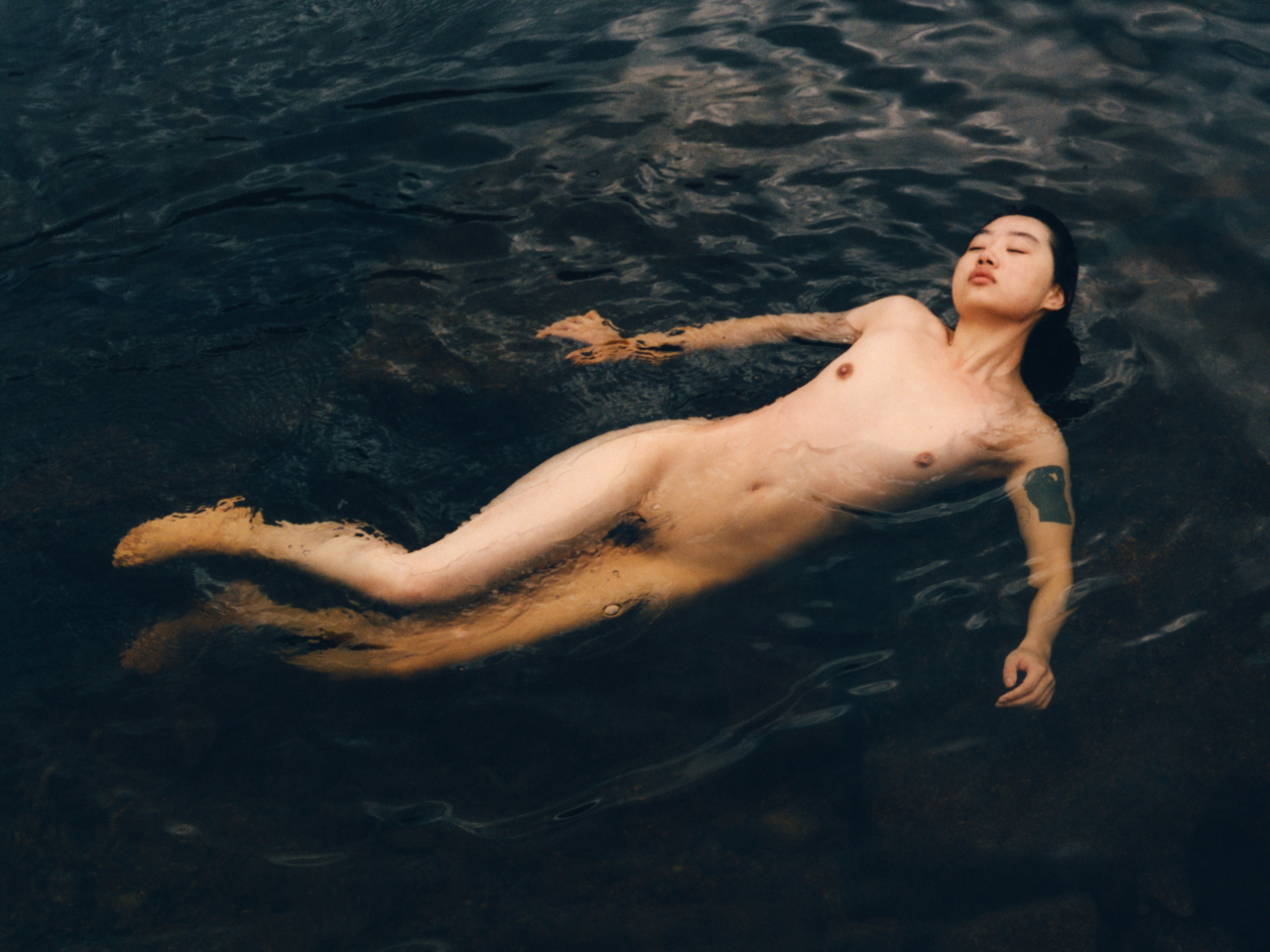 A nude model floats in a blue lagoon.