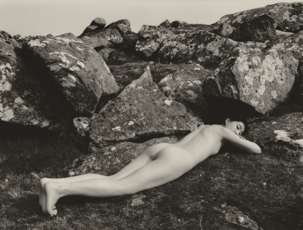 A model lays along the grass in front of a collection of large granite rocks.