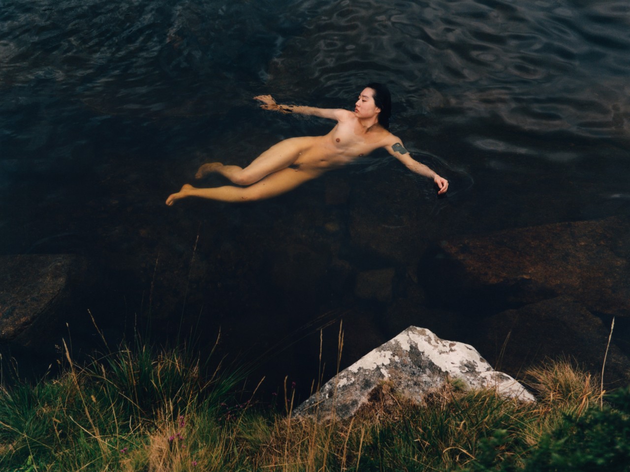 A model swims nude in a blue lagoon.