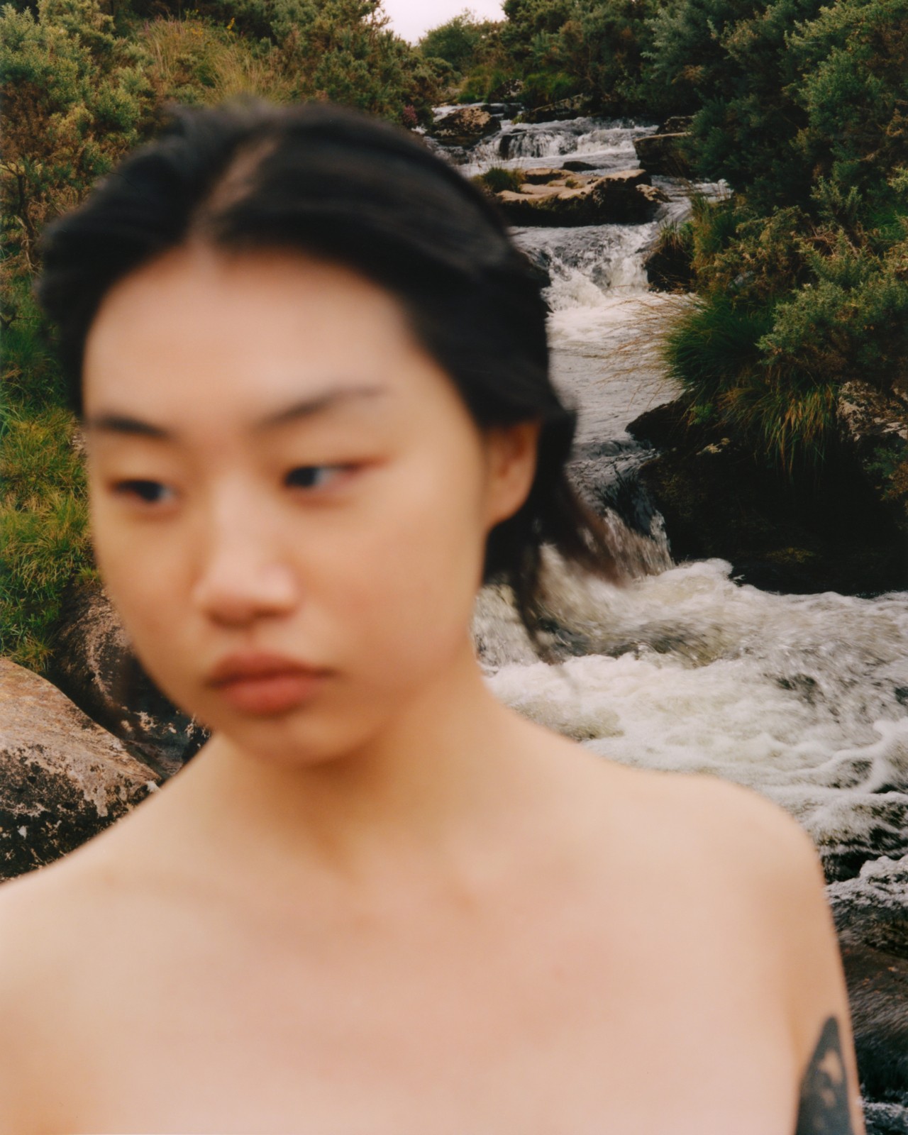 A model poses in front of a waterfall in the forest.