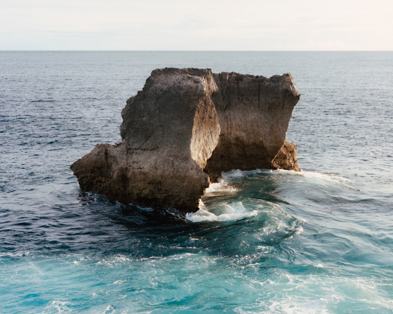 A large boulder sits in the middle of the ocean.