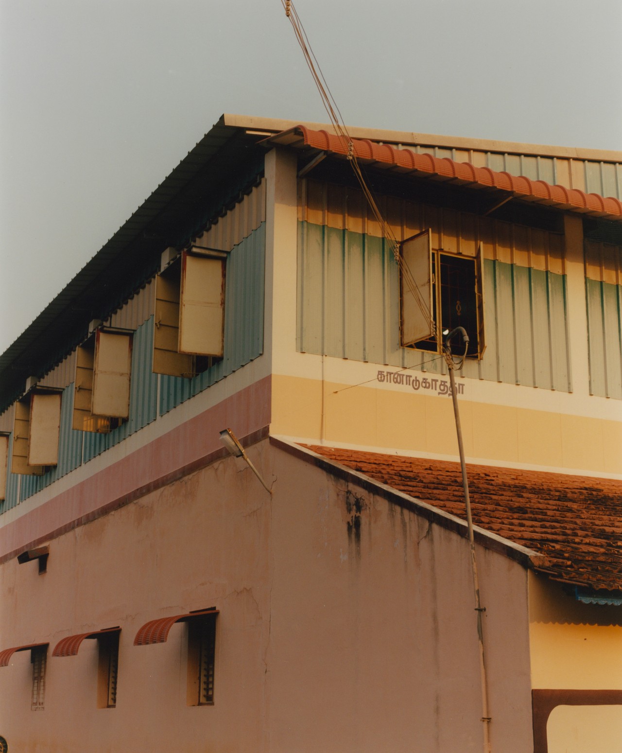 Several windows are open at the top of a light blue and beige house in Southern India.