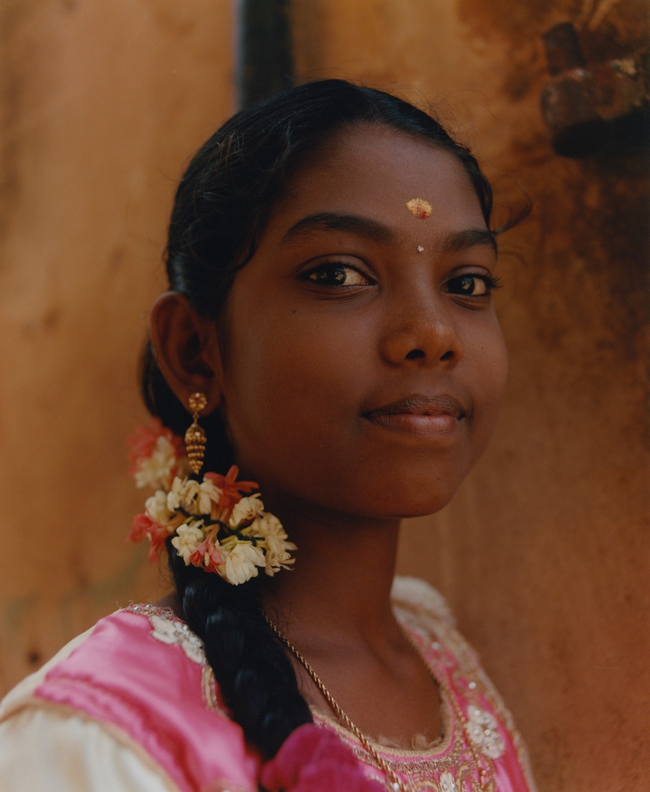 A young woman dressed in traditional Indian garb and a flower in her hair peers at the camera.