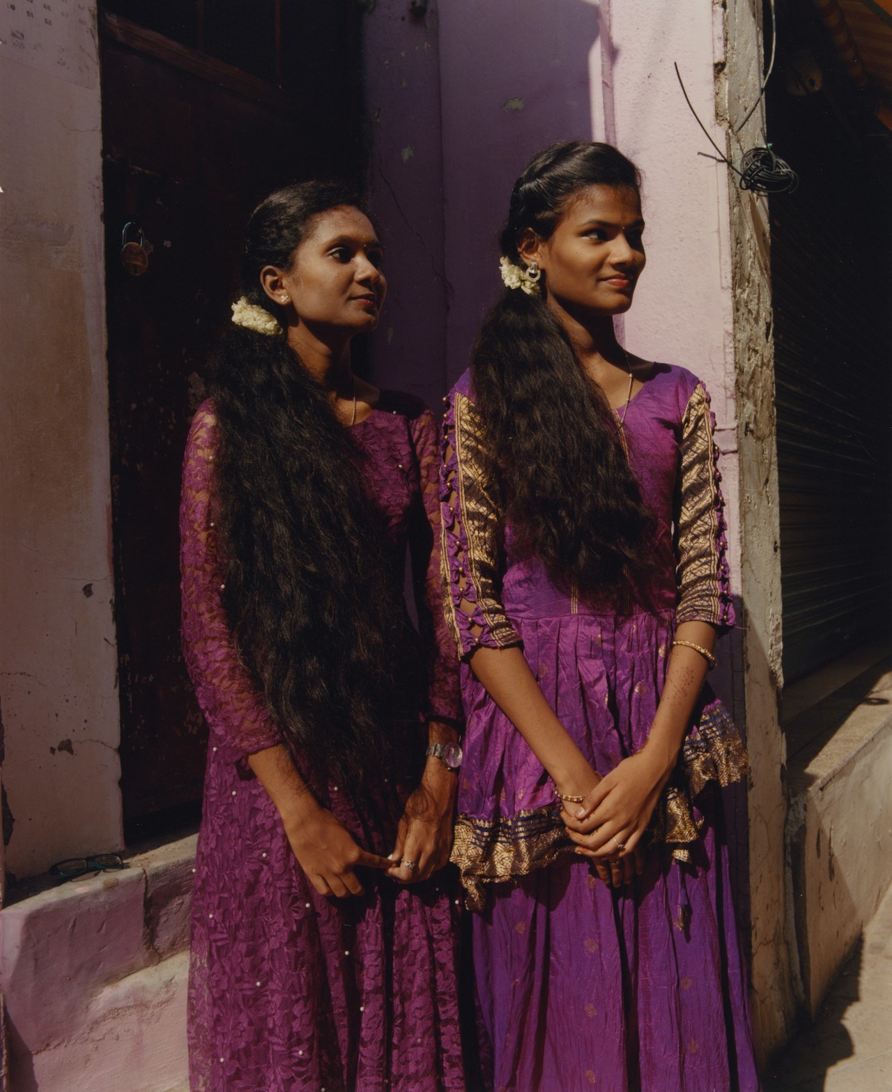 Two young women wearing matching purple dresses pose next to each other in Southern India.