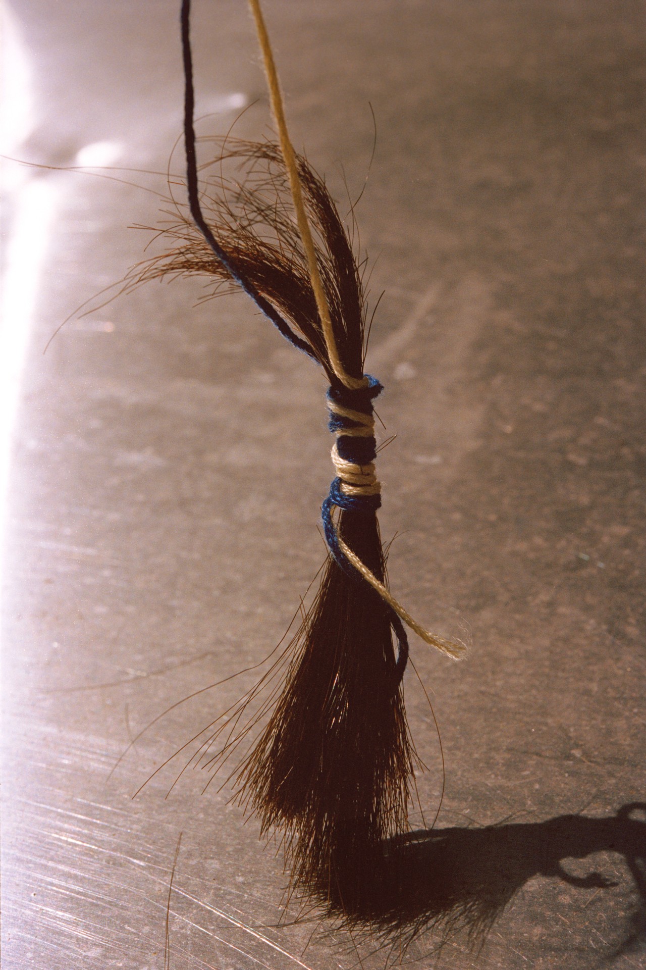 A piece of cut hair tied together by yellow and blue string hangs above a silver table.