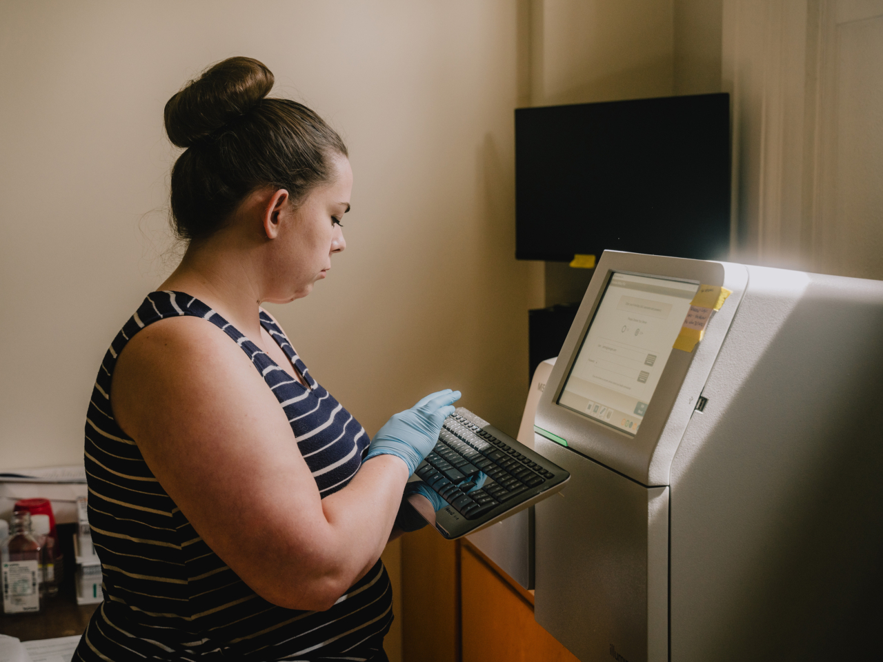 A person wears gloves while typing on a keyboard connected to a monitor in a forensics lab.