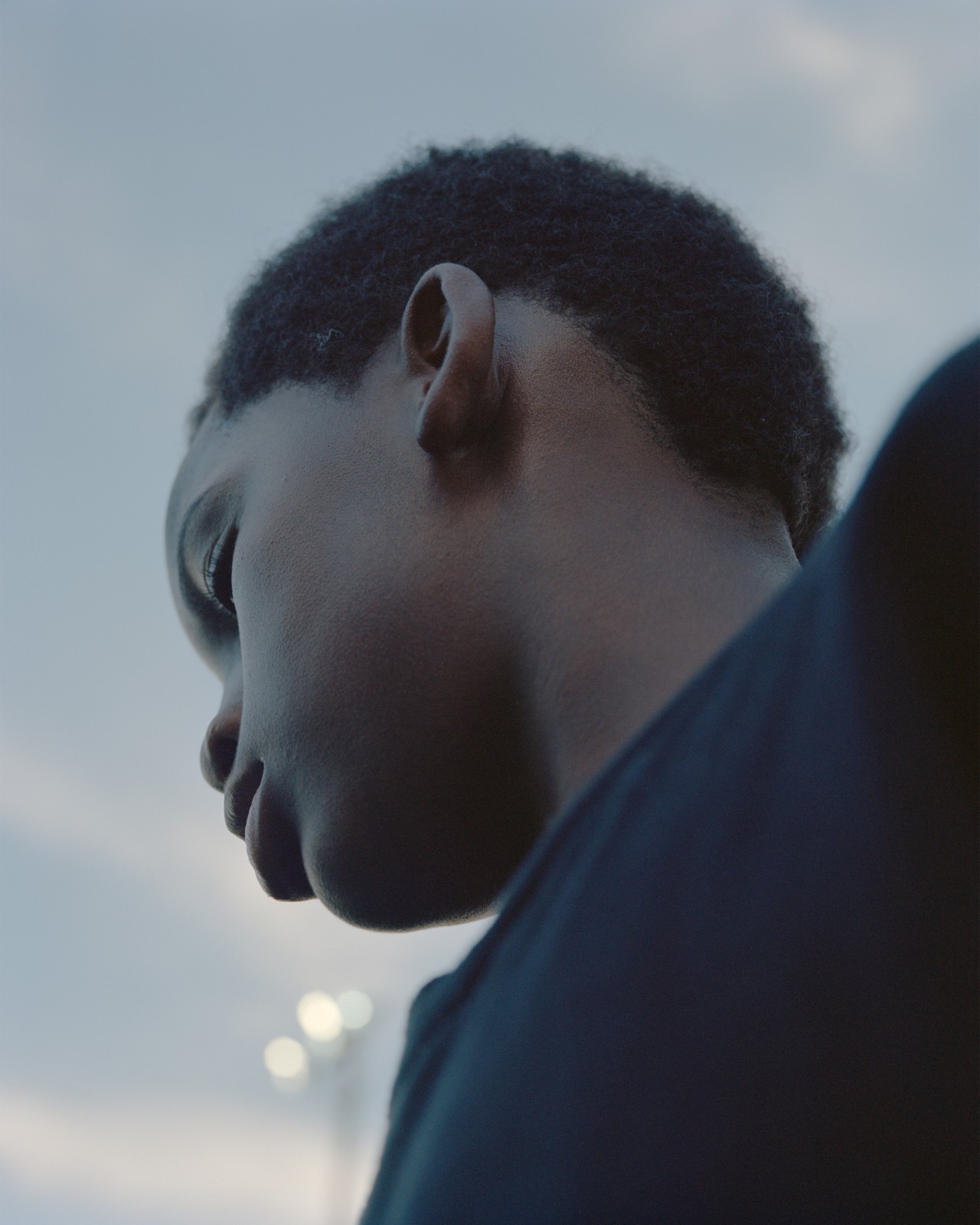 A young boy wearing a black t shirt looks down.