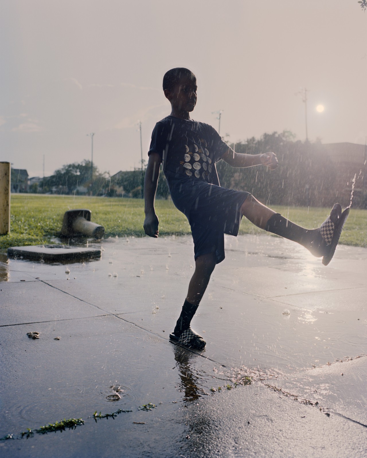 A boy kicks his foot up as it rains in a park.