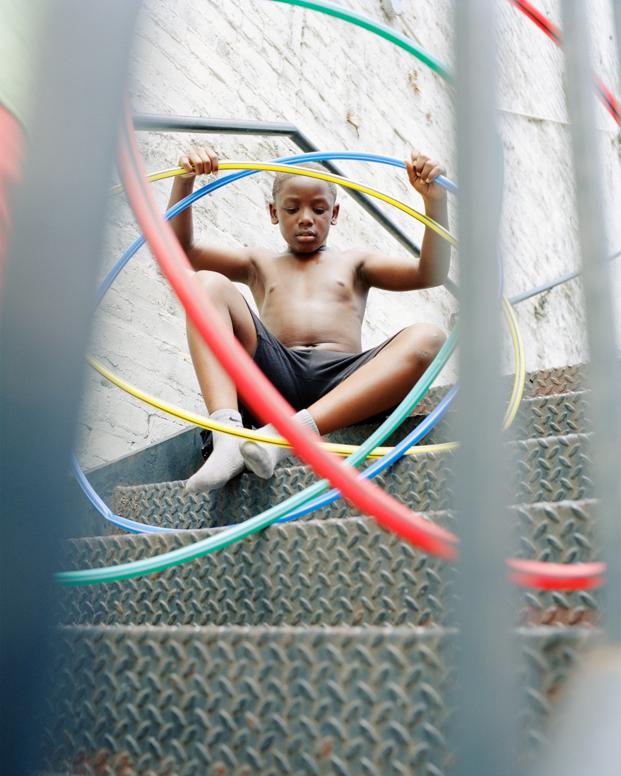 A young boy sits on a stair well holding multiple colored hula hoops.