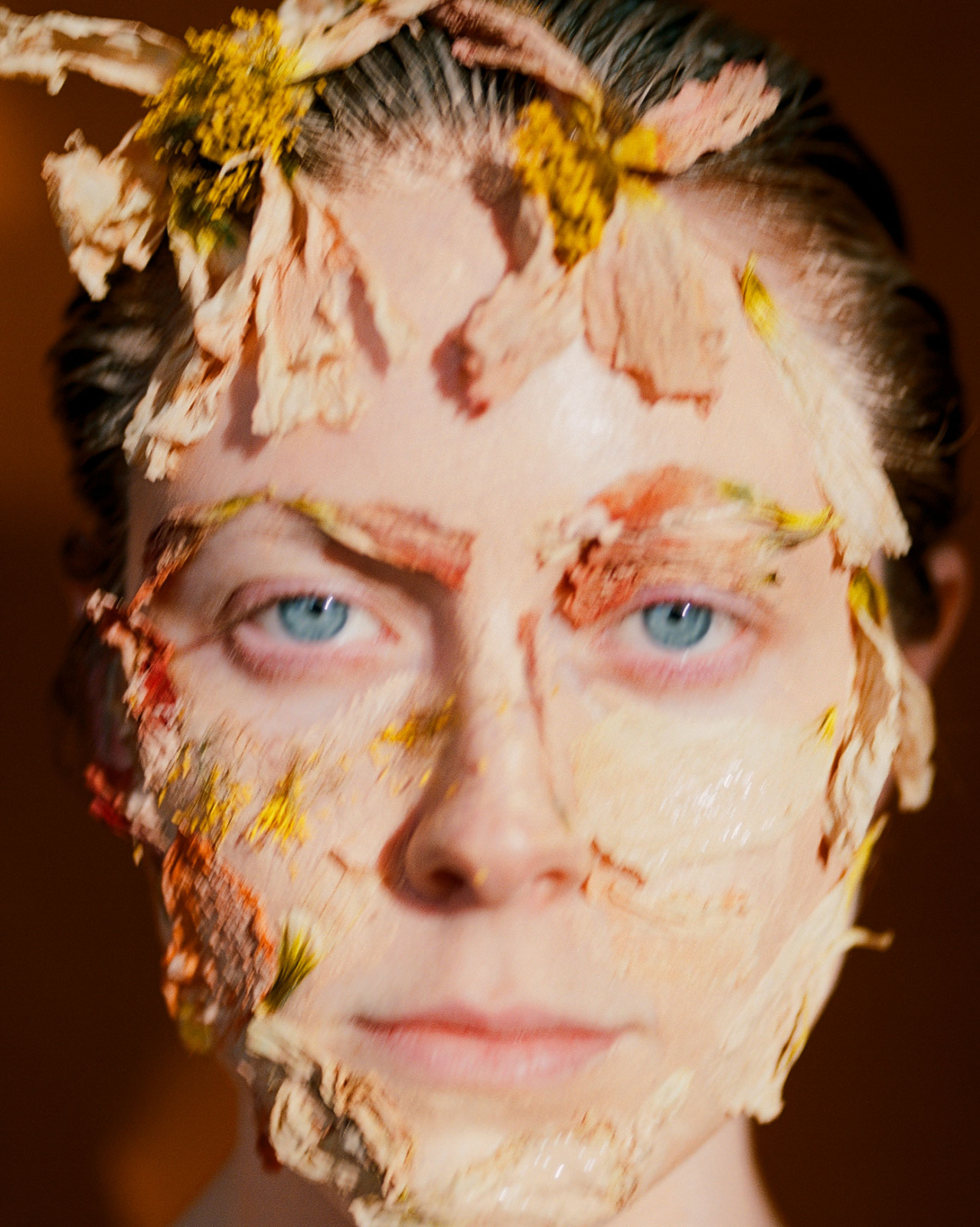A model stares ahead with flowers pasted to their face.