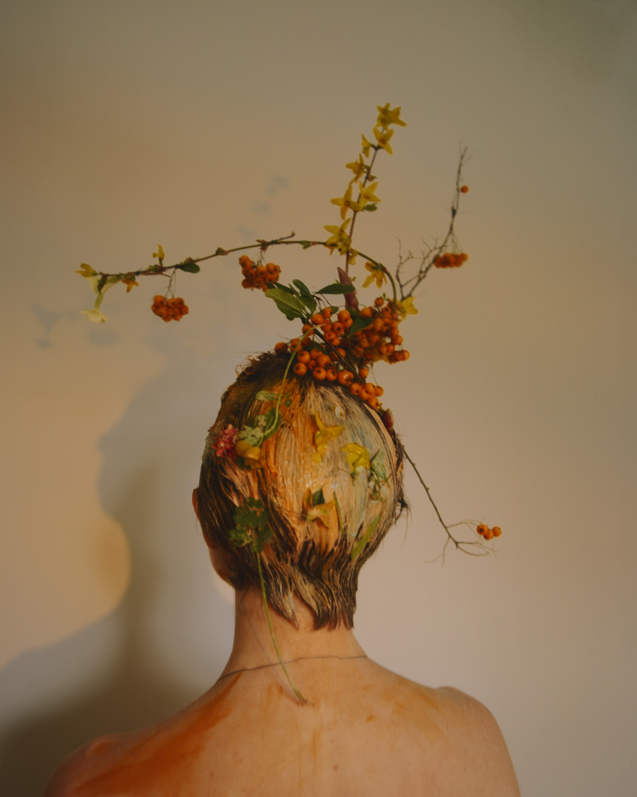 A model wears multi color paint in their hair and a plant atop their head.