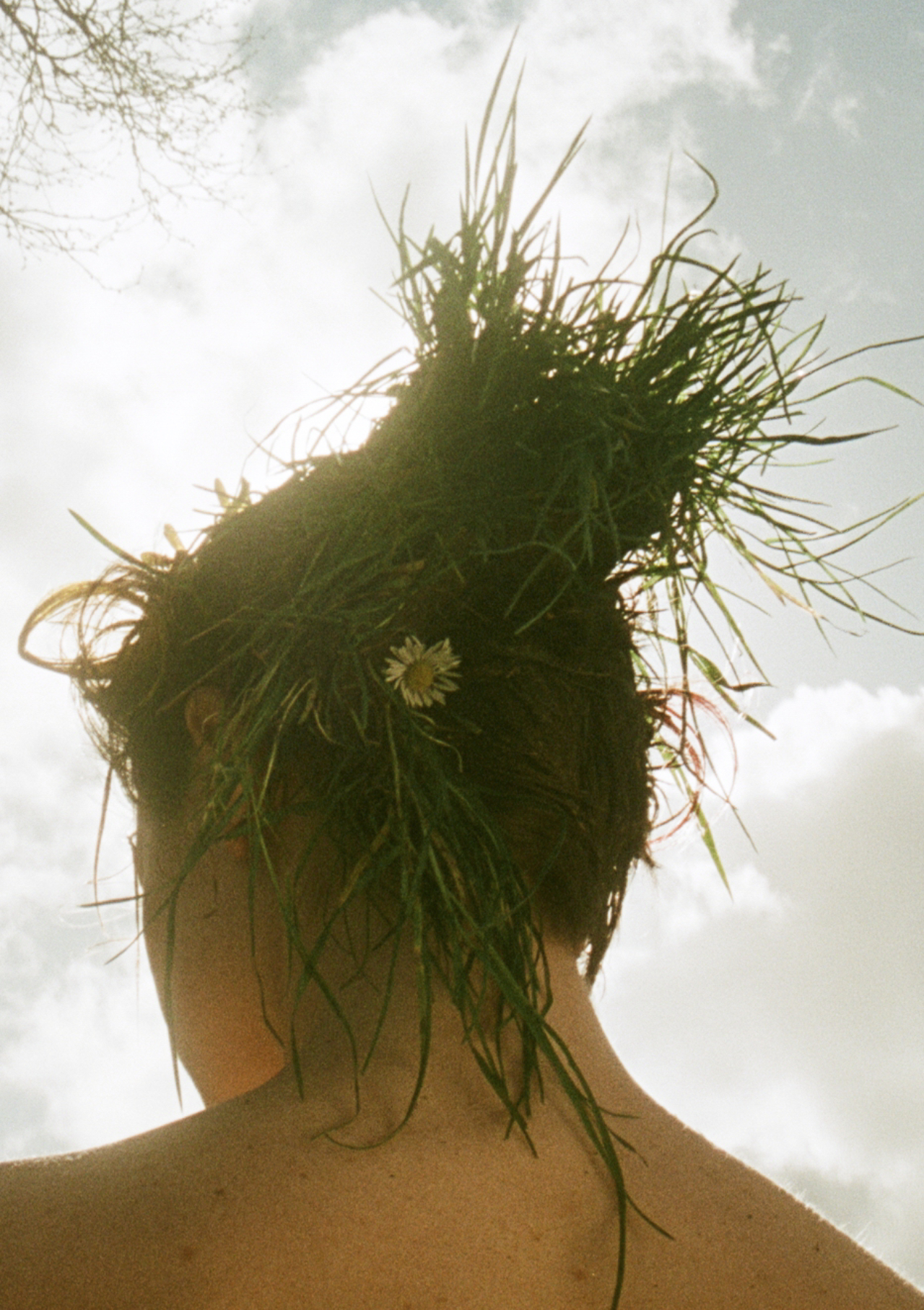 A model with grass and flowers on top of their head looks away.