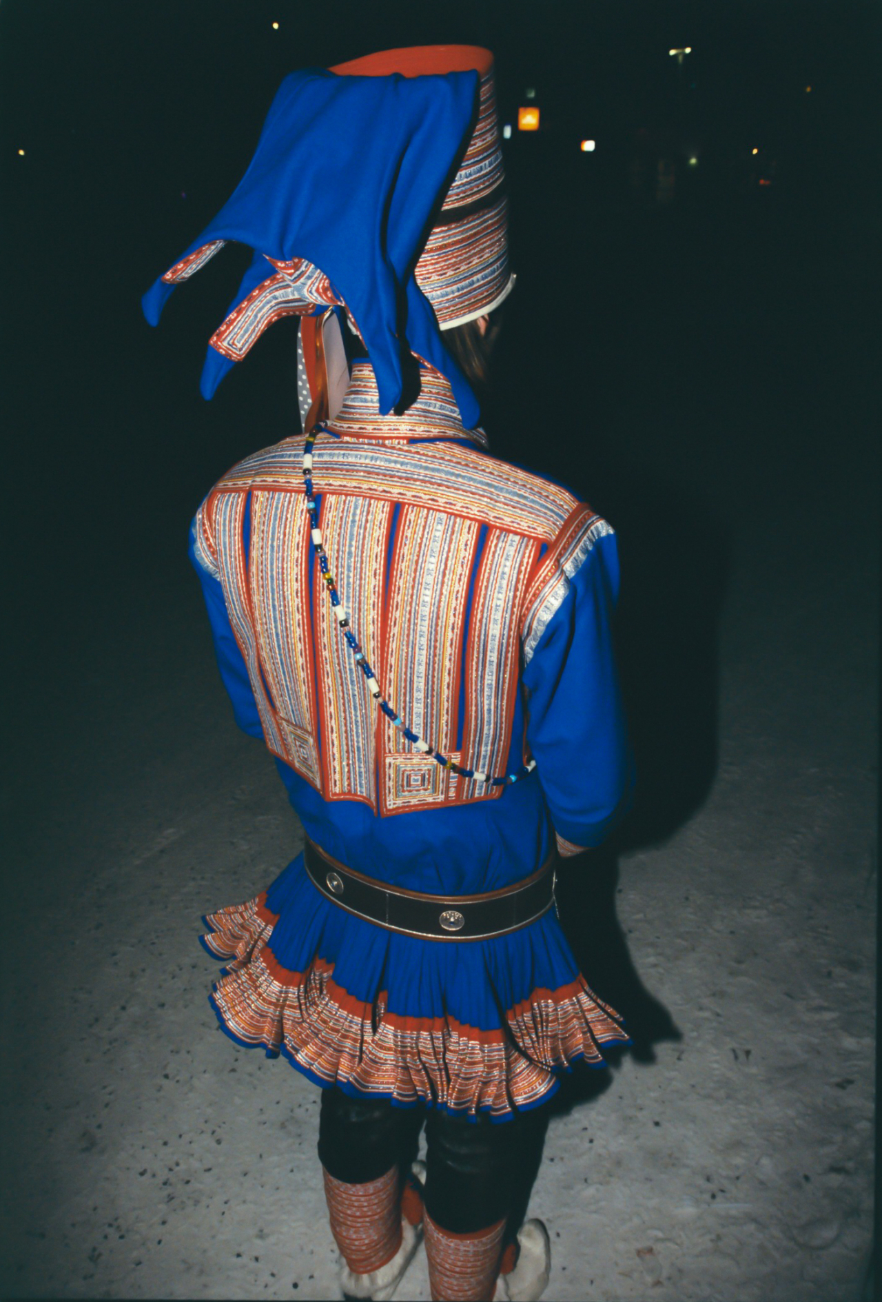 A person wearing traditional Sami people garb stands in the snow and faces away.