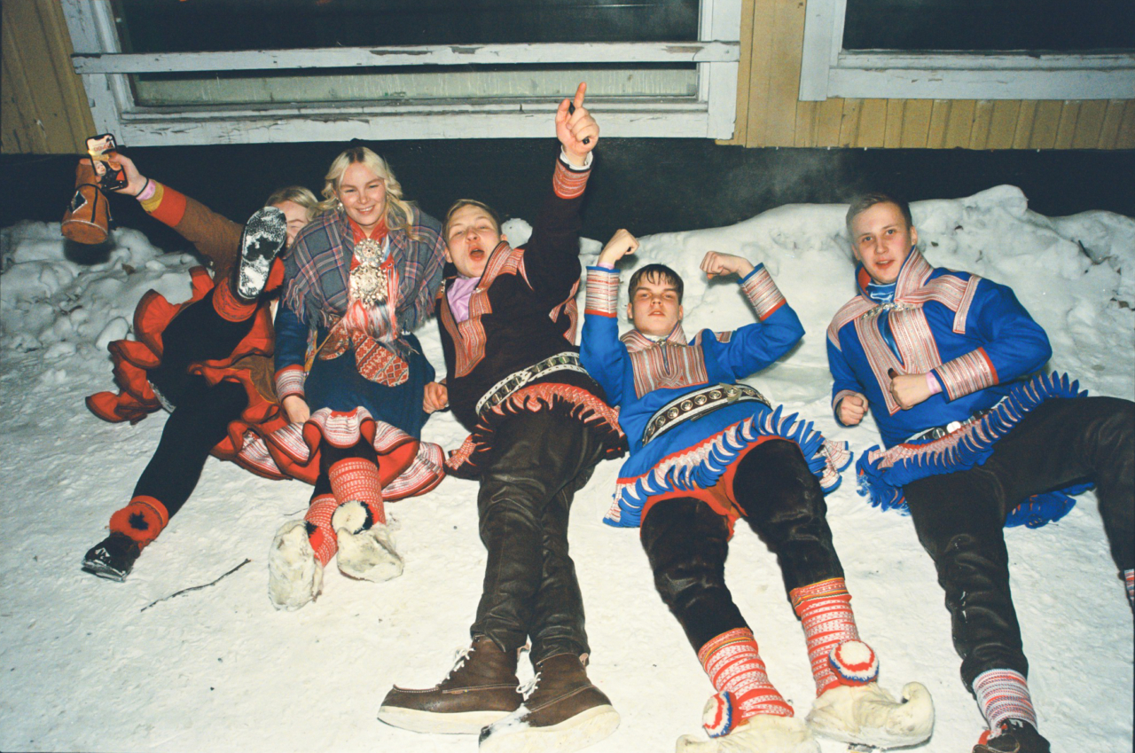 A group of Sami youth lay together in the snow.