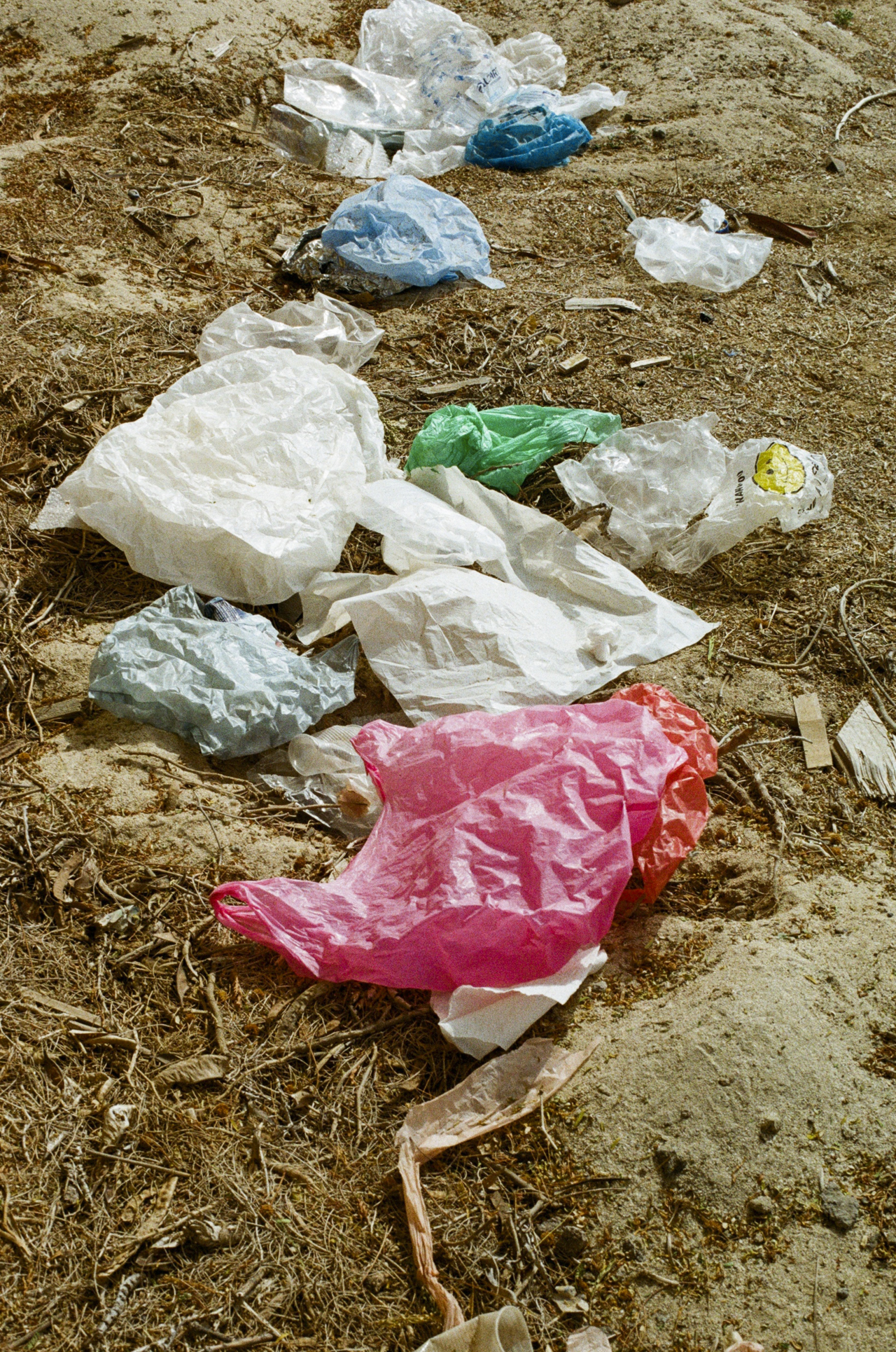 Different kinds of plastic pollution are spread across the dirt ground.