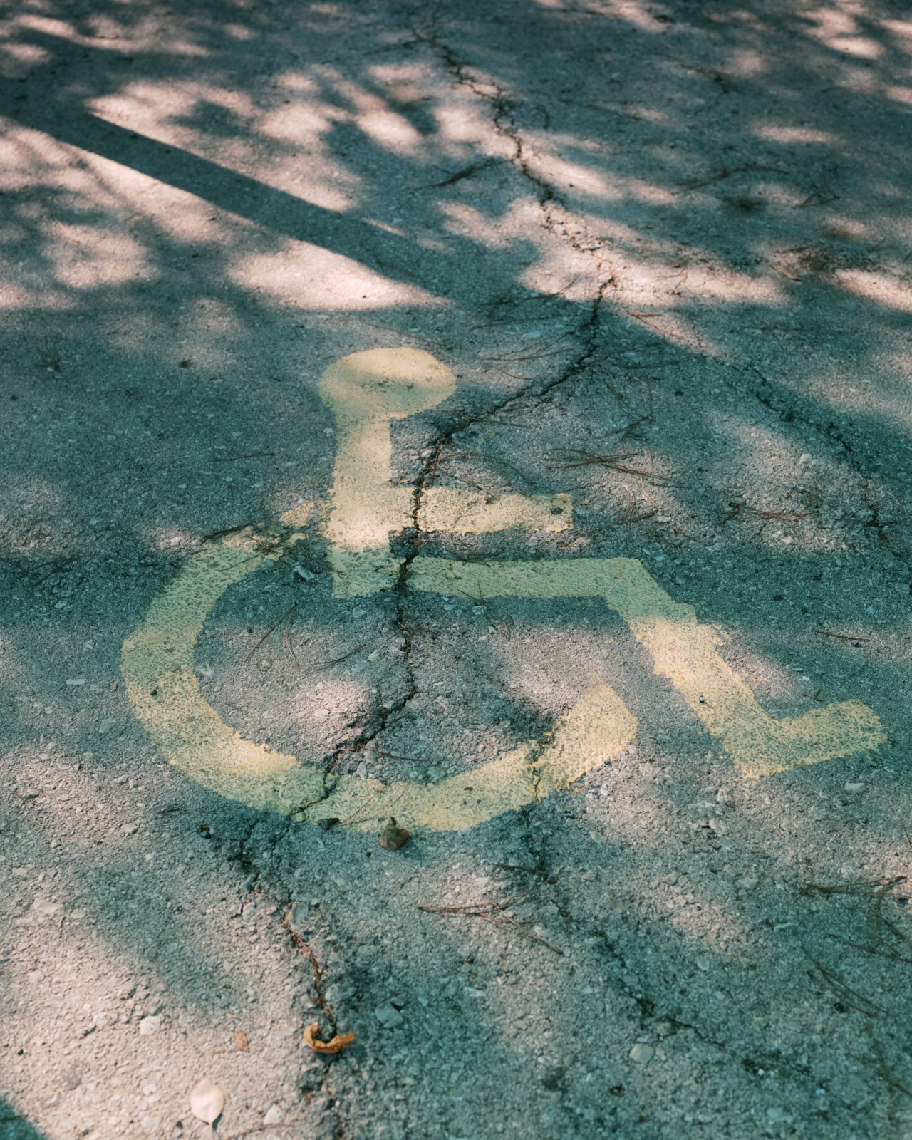 An image of a stick figure person using a wheelchair is drawn in yellow paint on a cement street.