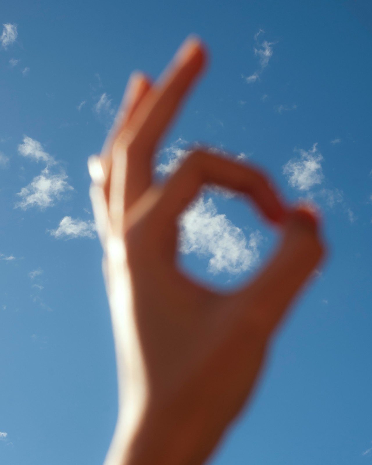 A hand makes a circle with their pointer finger and thumb in front of a blue sky