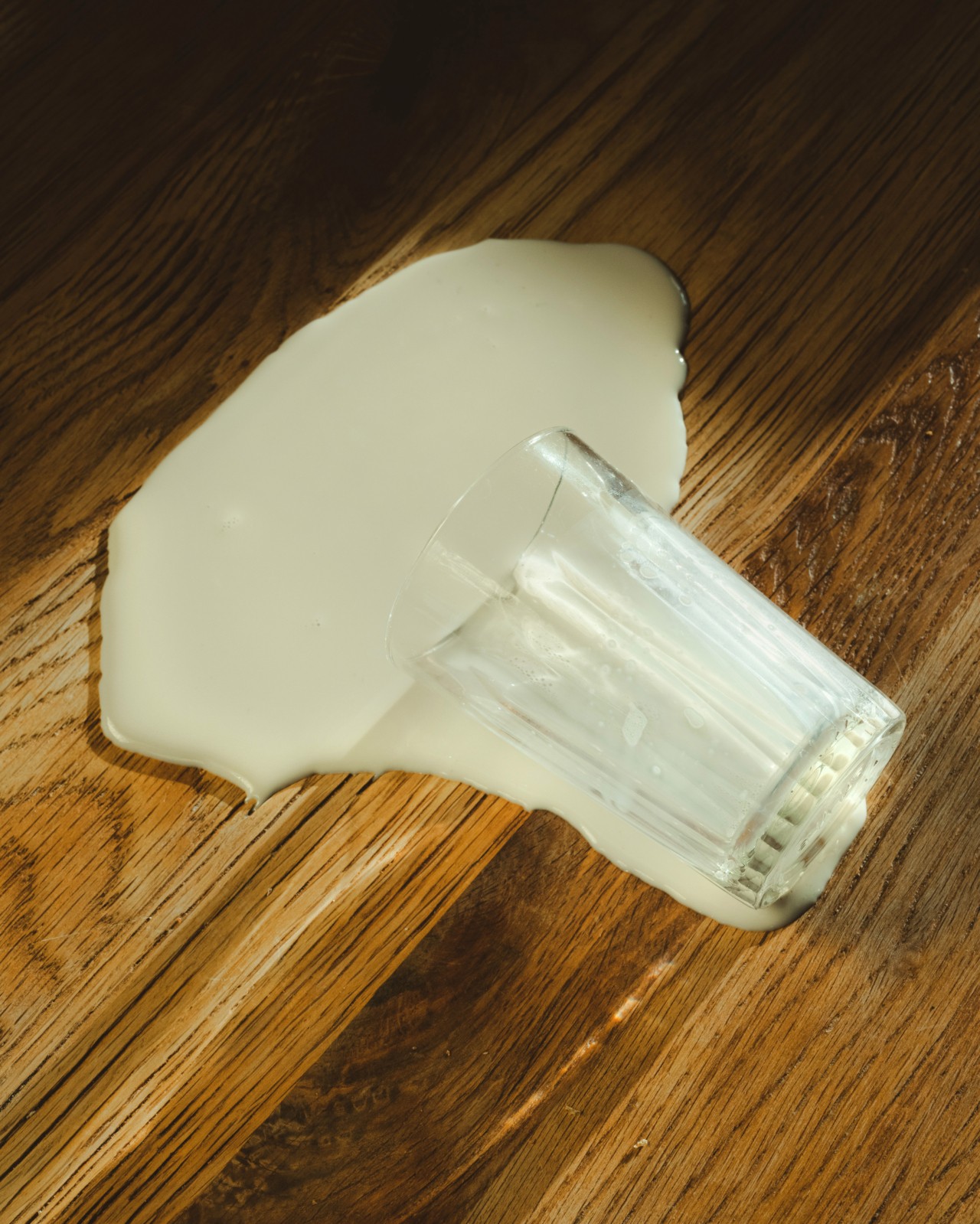 A glass of milk spills onto a mahogany wood surface.