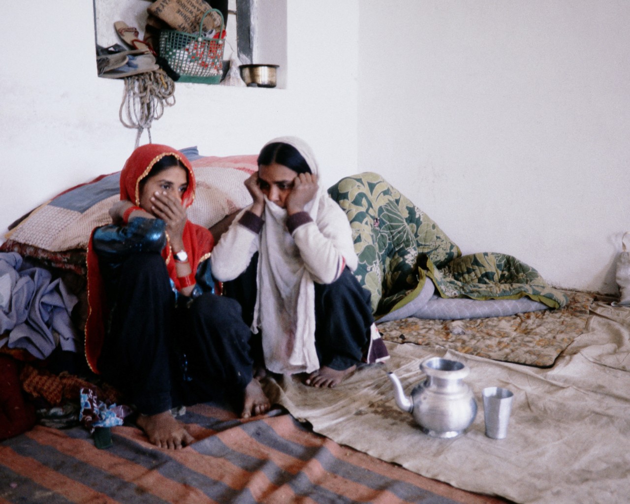 Two women in India sit together on a floor covered in blankets.