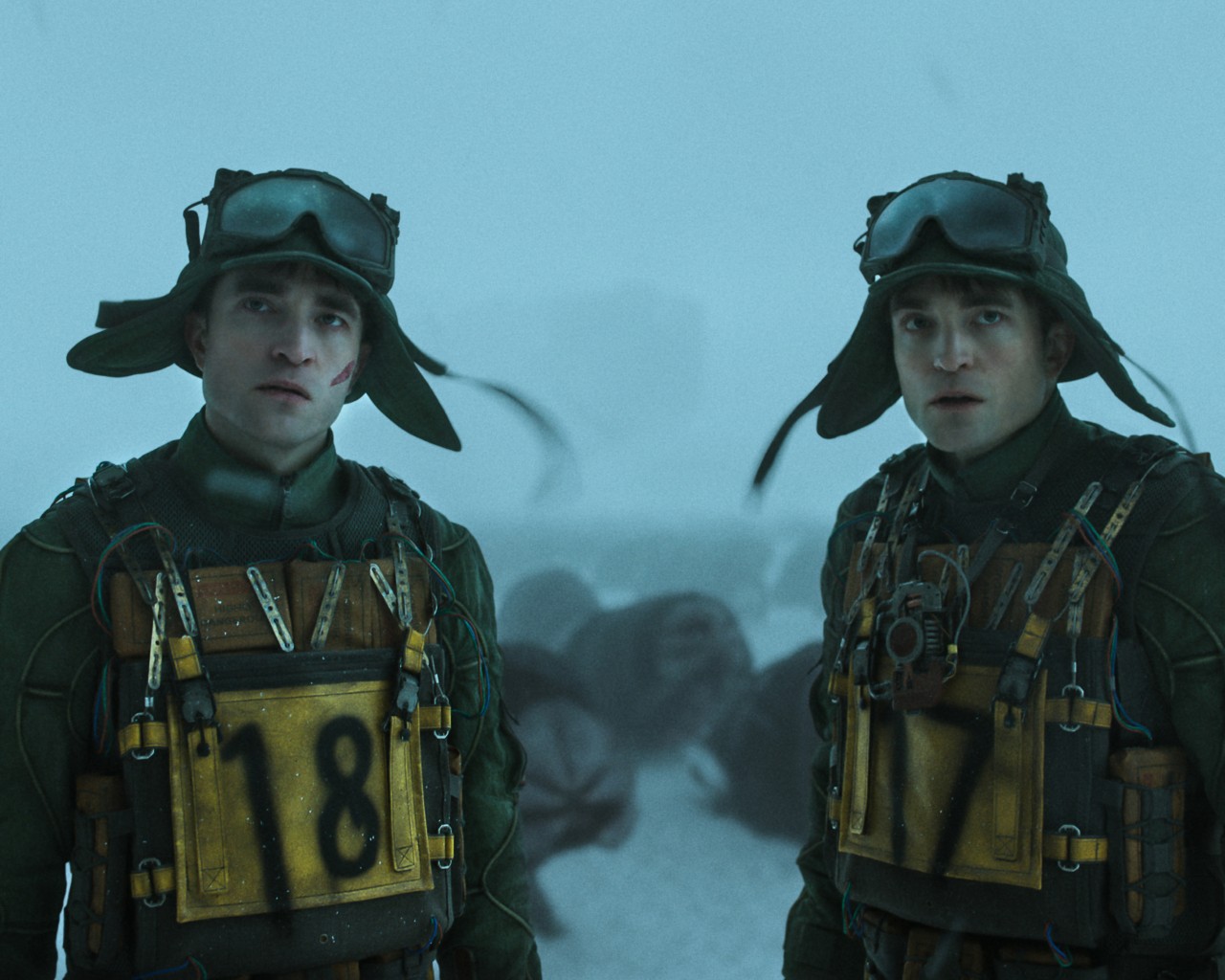 Robert Pattinson and his clone, both whom are dressed in space gear, stand side by side.