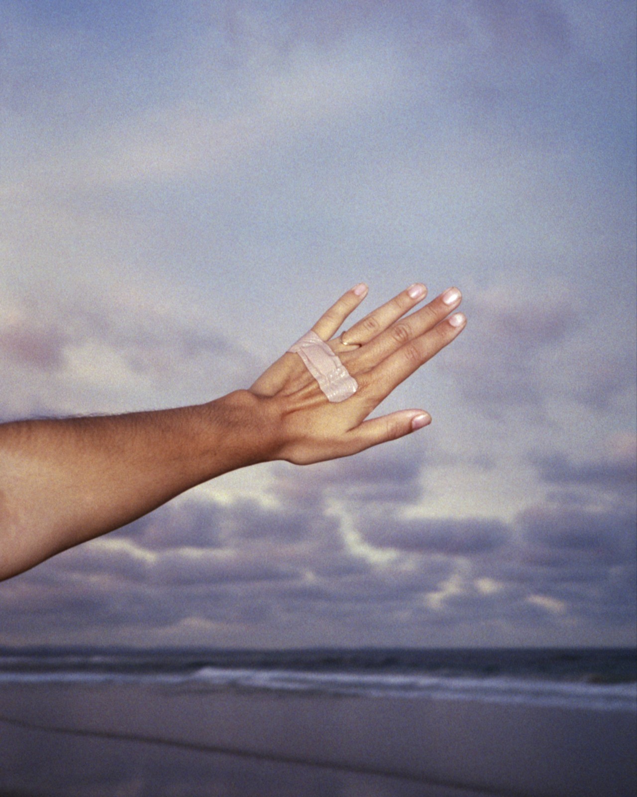 A person places their hand with a band aid across in front of a cloudy sky and coastline.