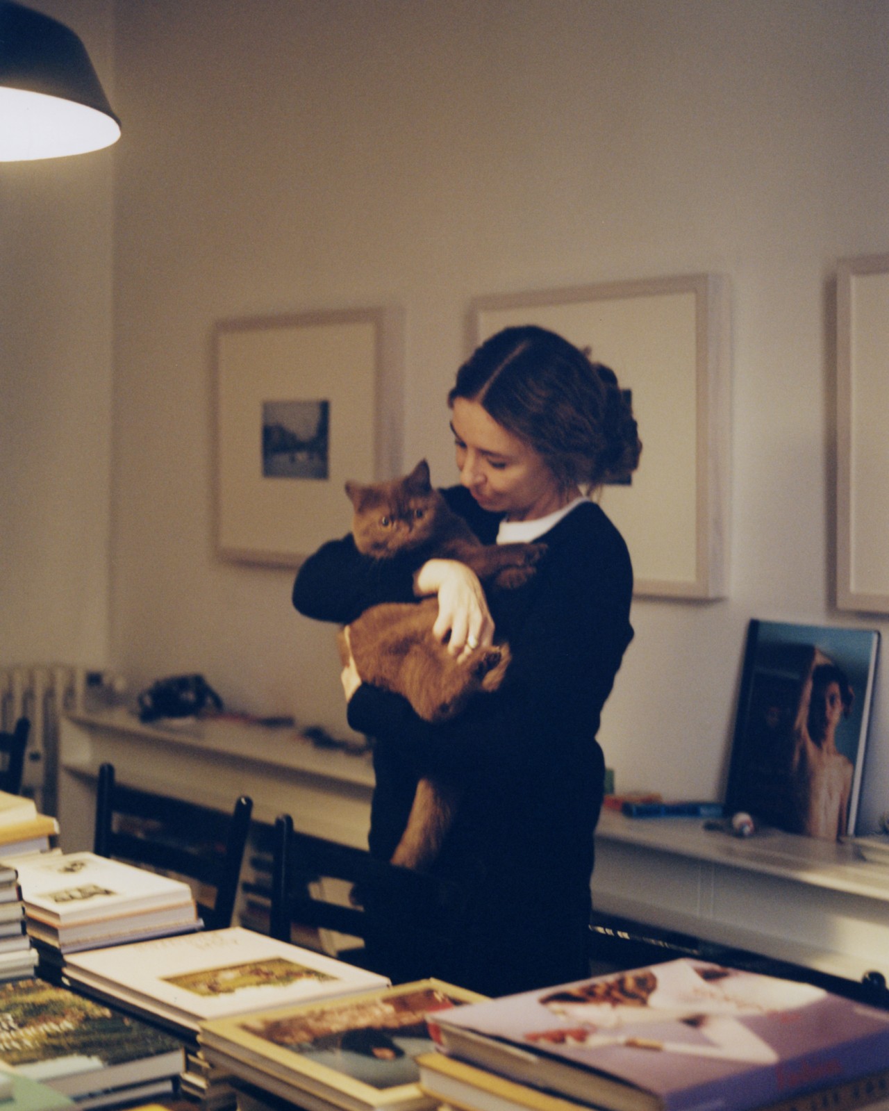 A woman holds a cat while looking at framed photography.