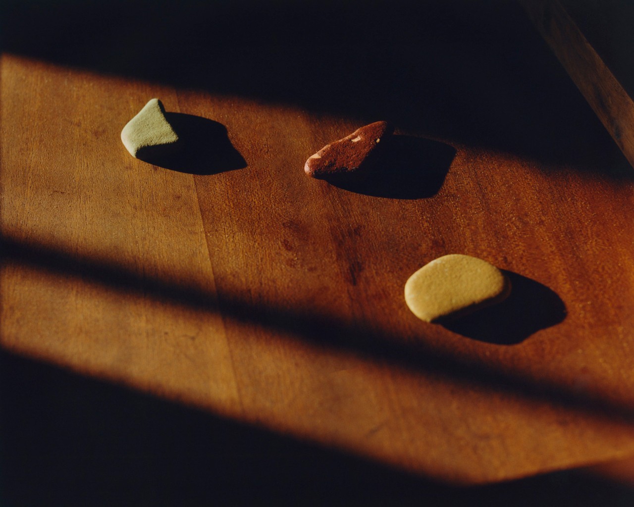 Three small rocks (green, red, and yellow) lay still on a wooden surface.