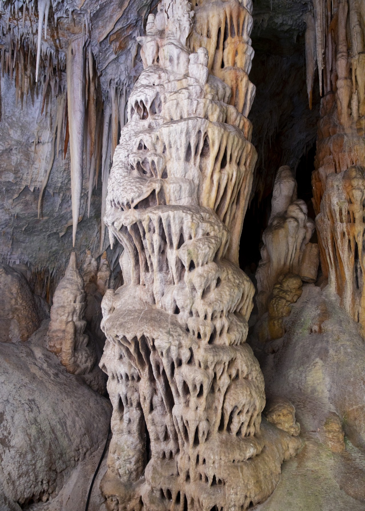 A large rock with patterned holes stands inside a cave.