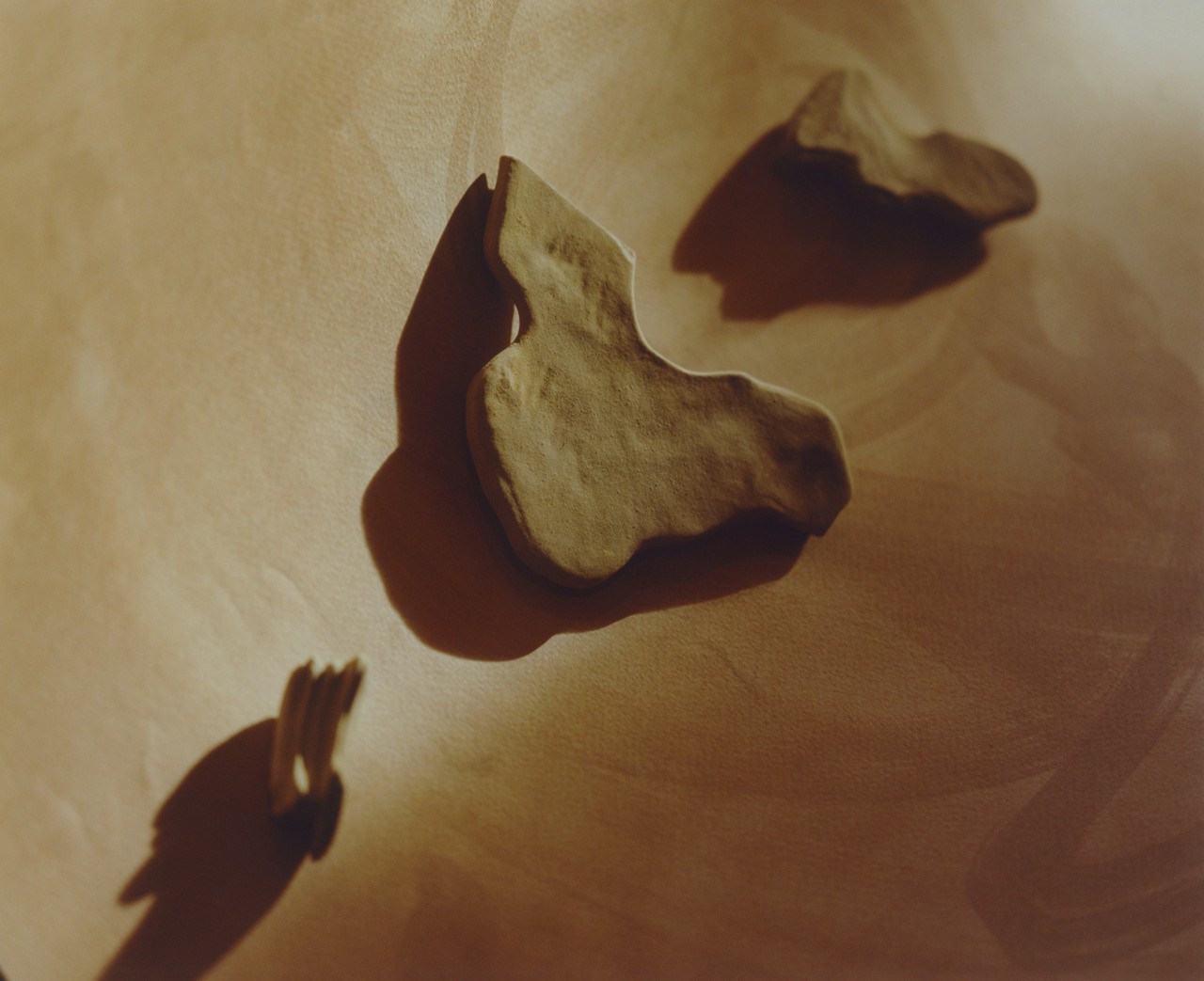 Three carved objects made of stone lie on a light brown surface.