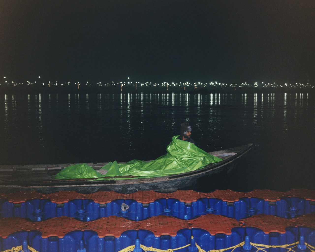 A boat rider rests inside a boat at Triveni Sangam during sunset.