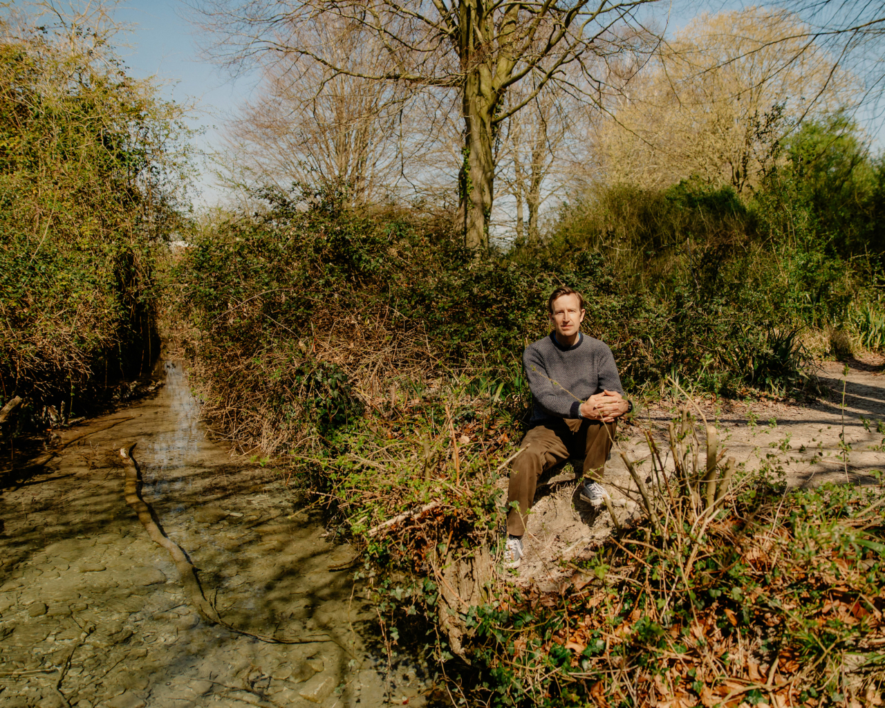 Robert Macfarlane sits along a river in the U.K.