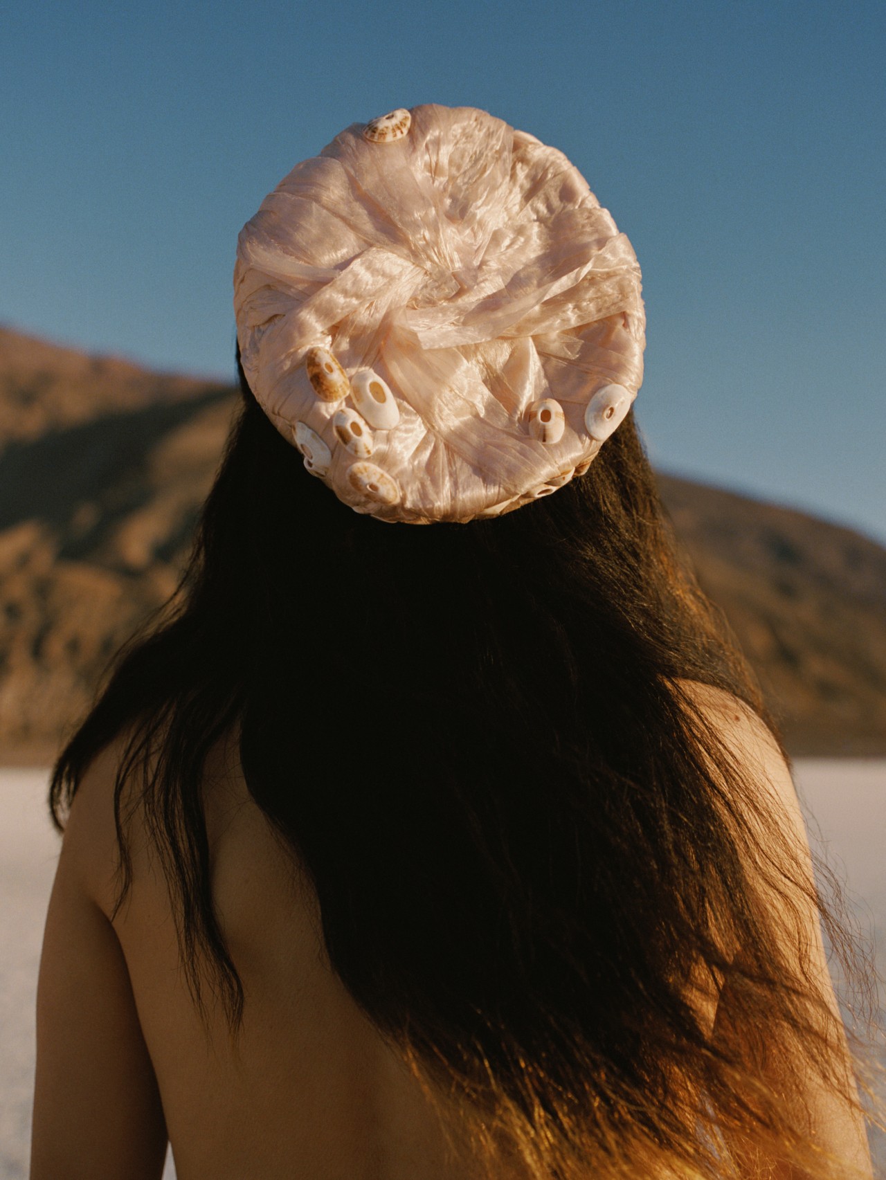 A person with long brown hairs wears a pink hat as they face away from the camera.