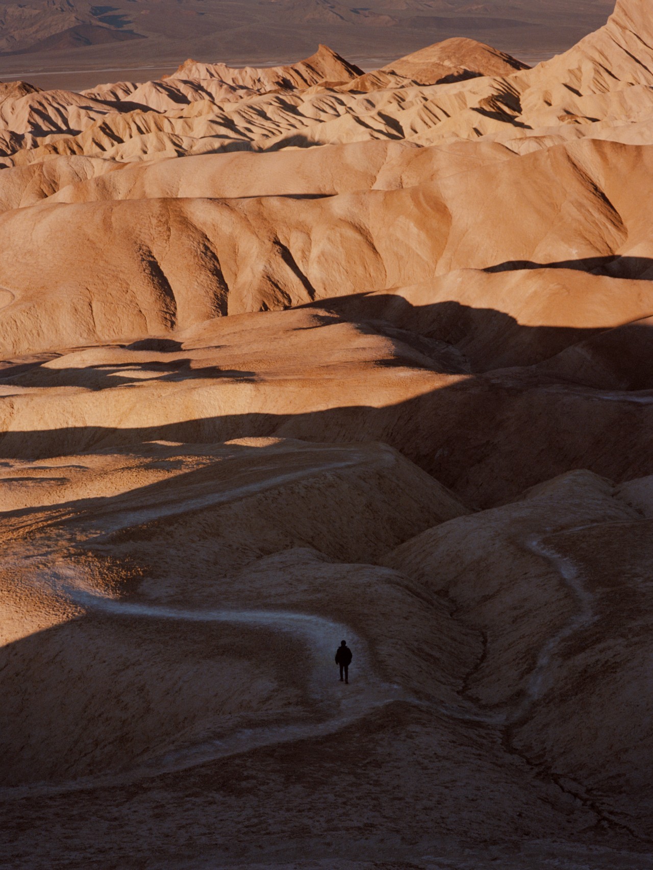 A lone person traverses the paths of a sandy mountain.