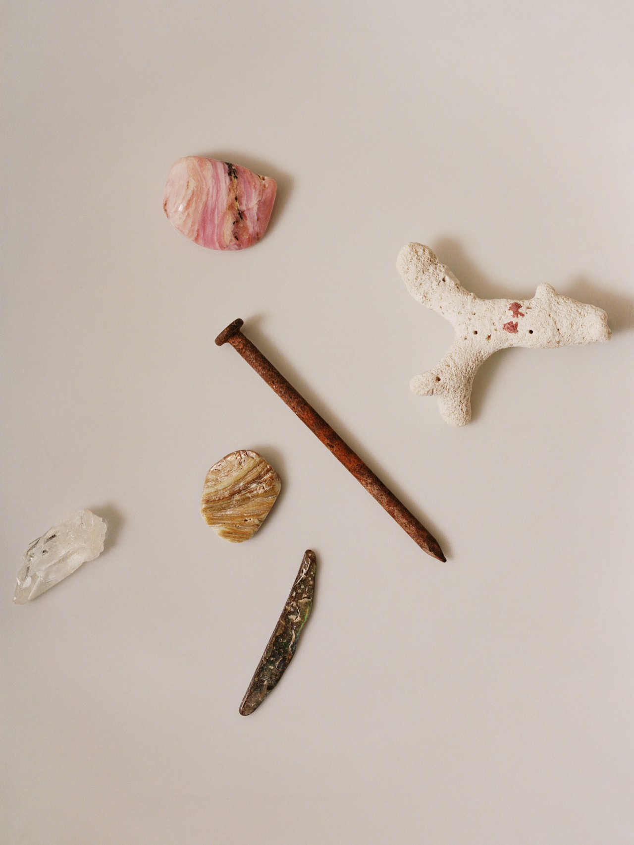 A rusty nail lays on a white table surrounded by small rocks of different shapes and colors.