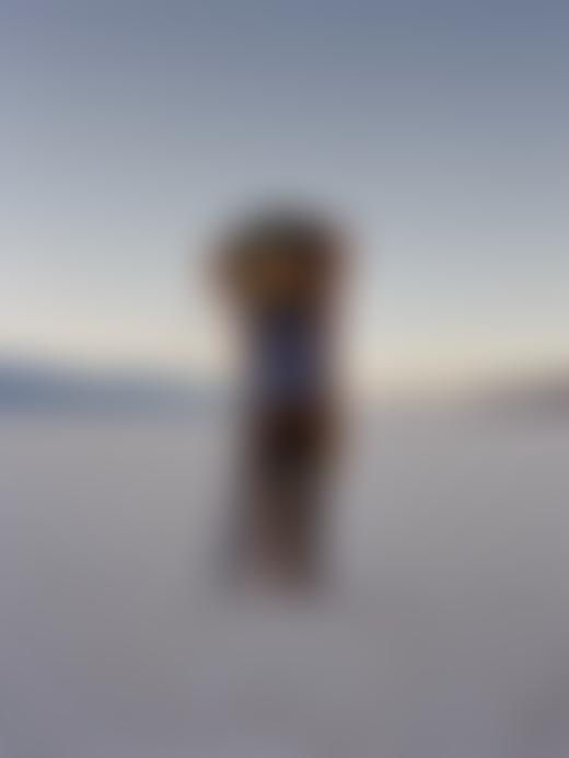 Someone stands in a vast landscape and covers their face and body with a multi-colored tunic.
