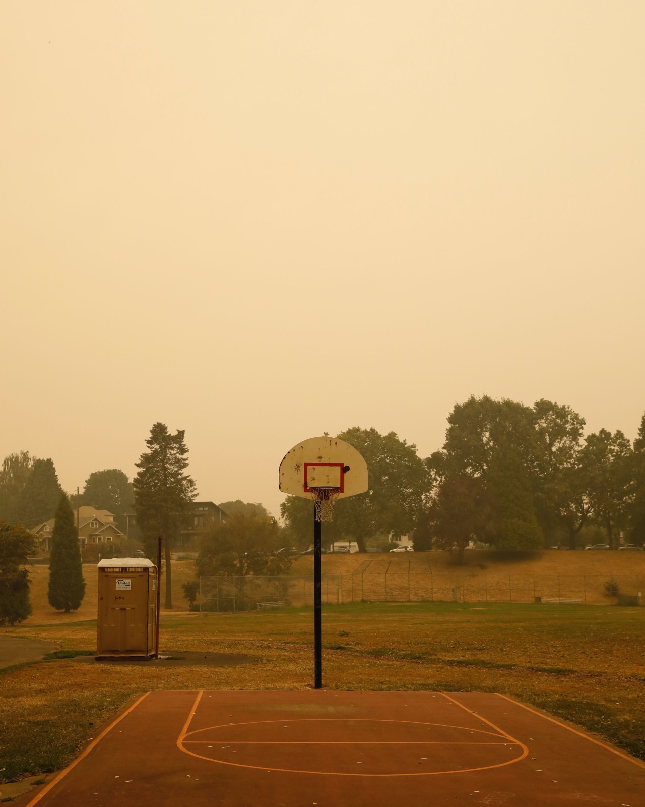 An old outdoor basketball hoop under orange skies caused by wildfire smoke.
