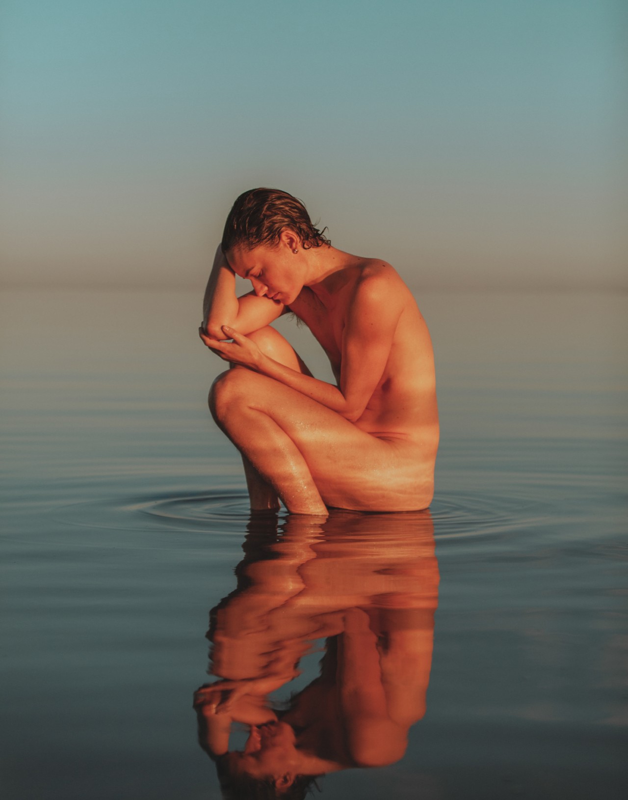 A person sits in the shallow water of the Salton Sea.