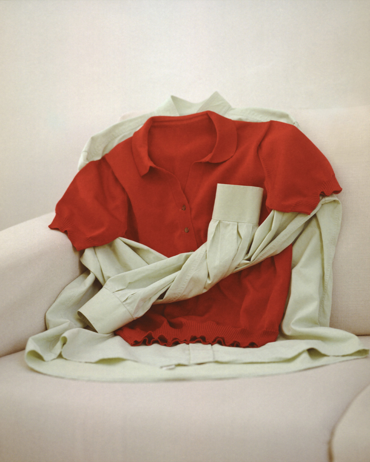 A red polo shirt is draped over a light green button-up shirt on a beige couch.