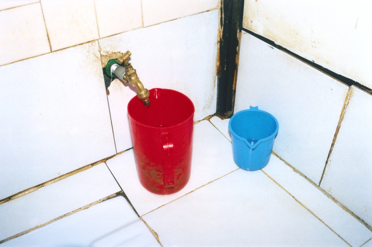 A red and blue bucket sit on the dirty tiled floor.