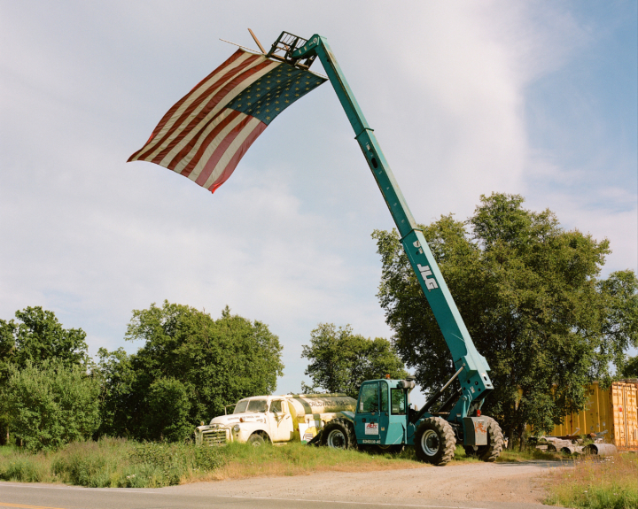 A crane carries an American flag in the countryside.
