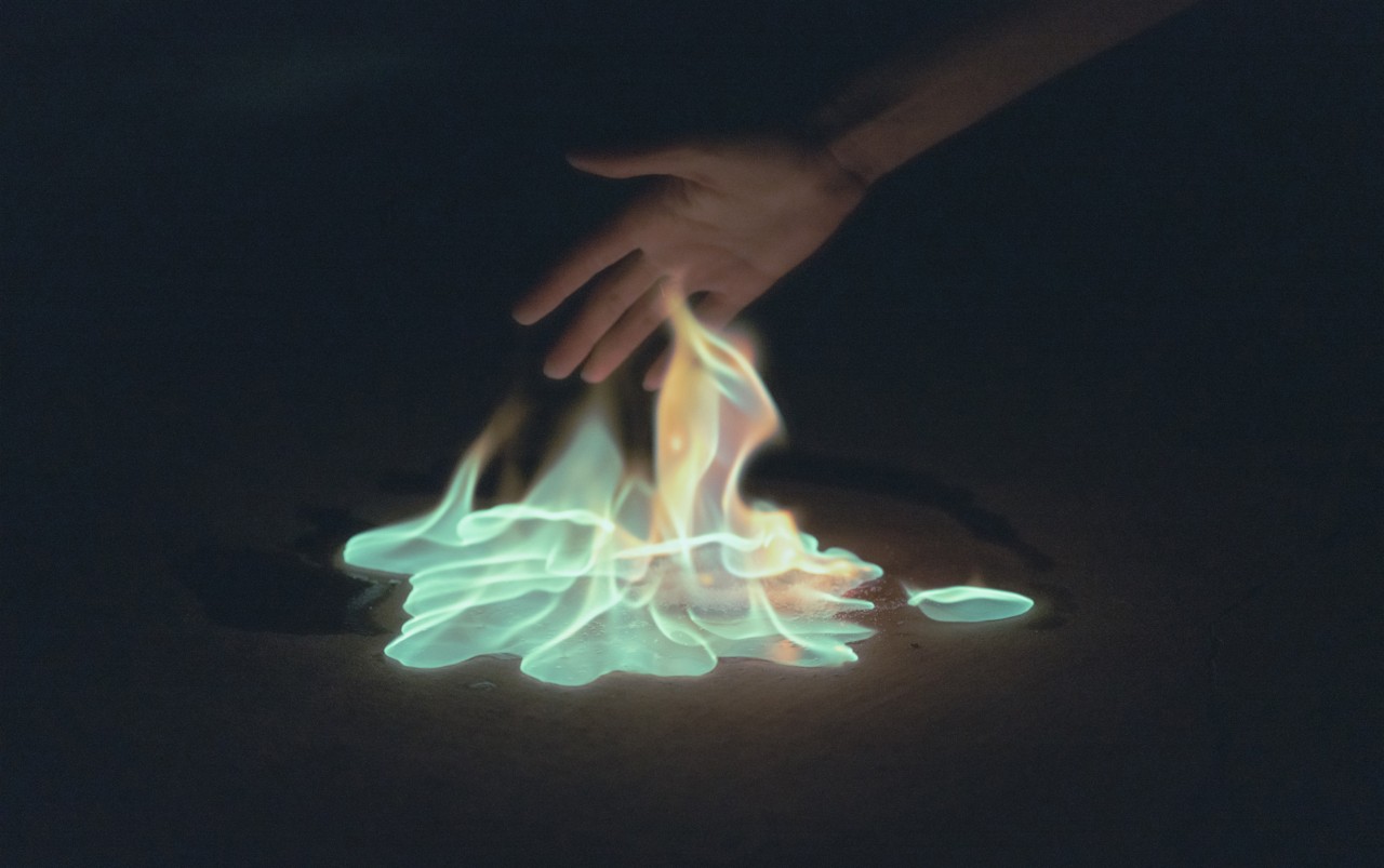 A hand hovers over an orange and blue flame.