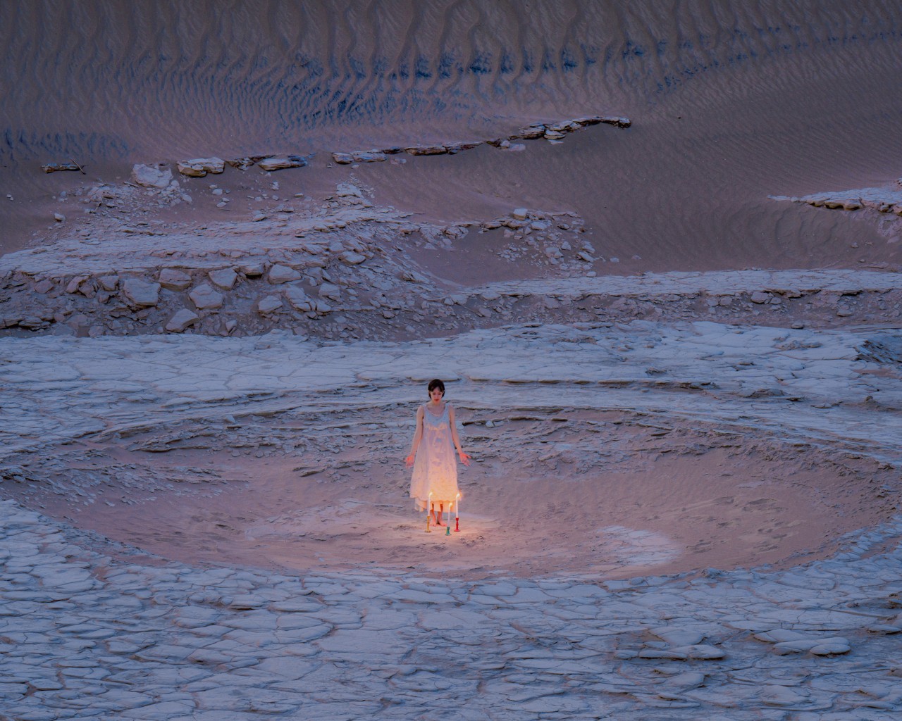 A person stands in the middle of a rocky landscape with candles surrounding their feet.