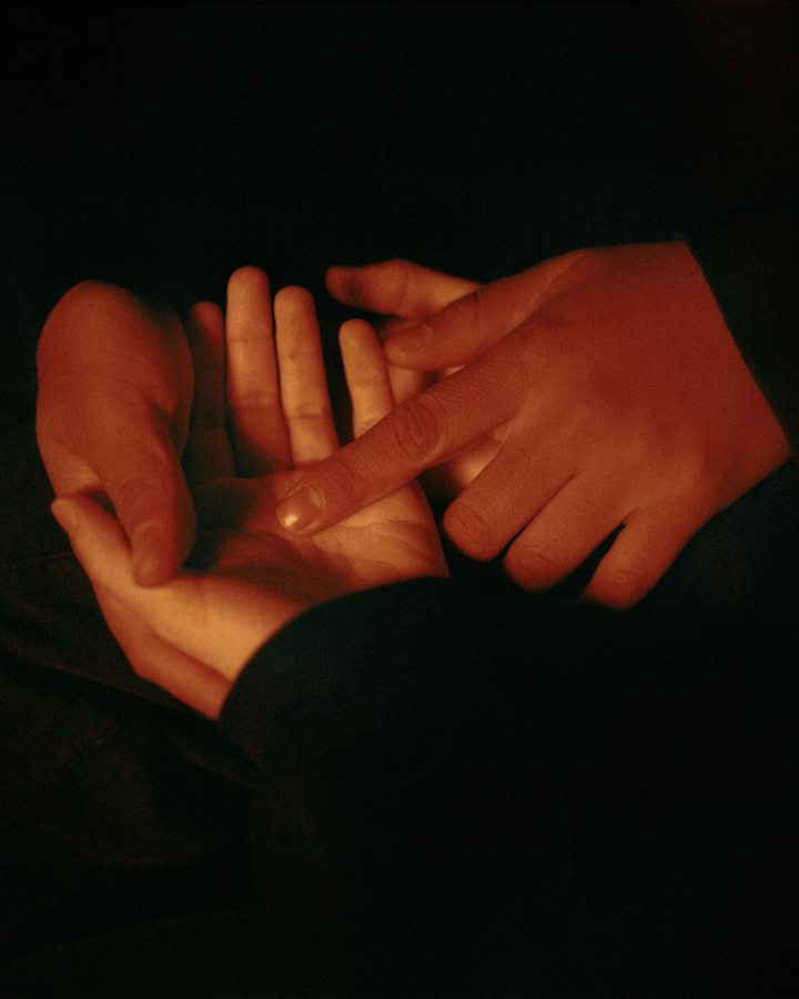 A person's pair of hand holds another person's palm open and touches it with their index finger.