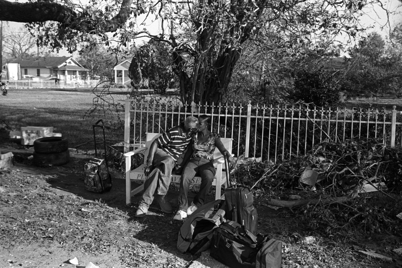 A couple shares a kiss on a bench amid packed luggage and storm debris after Katrina.