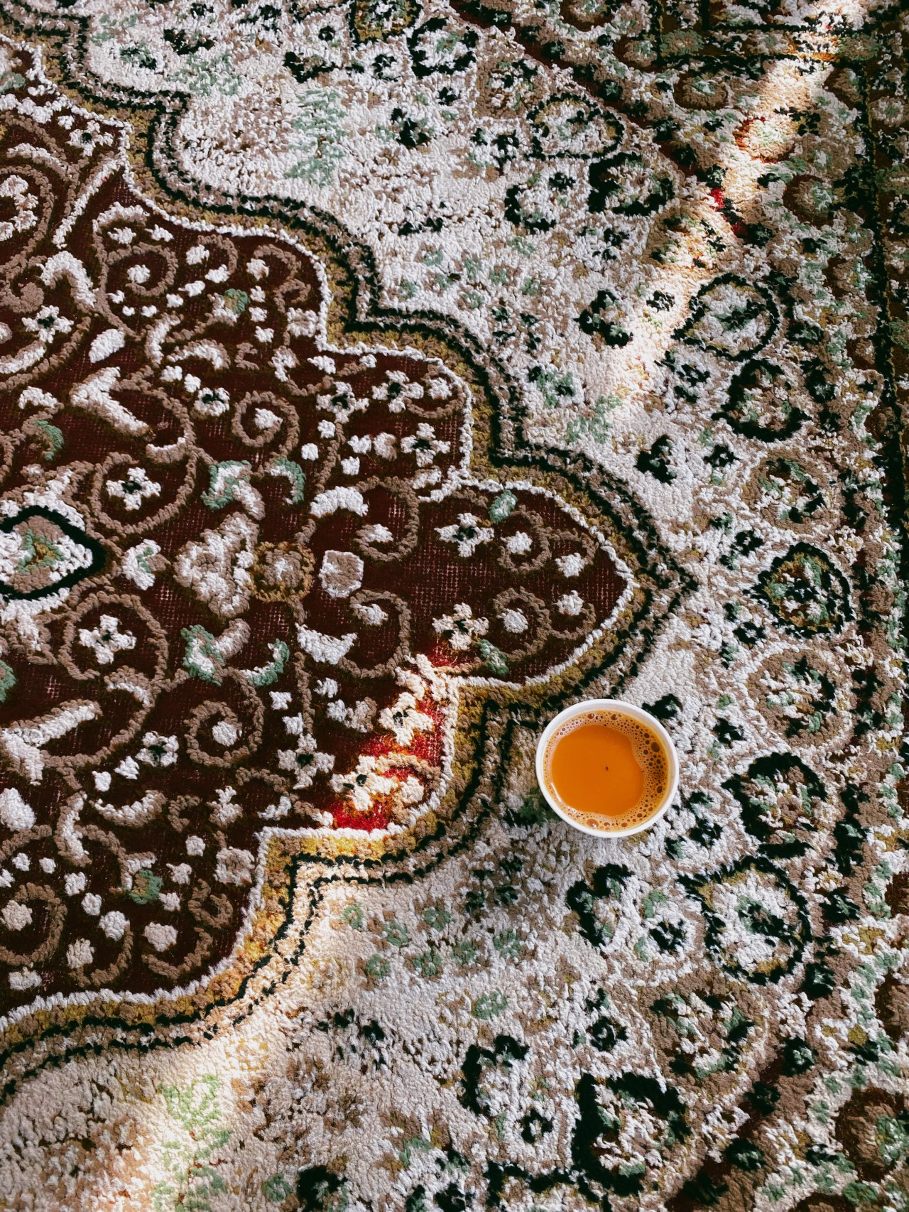 An orange drink sits on top of a rug.