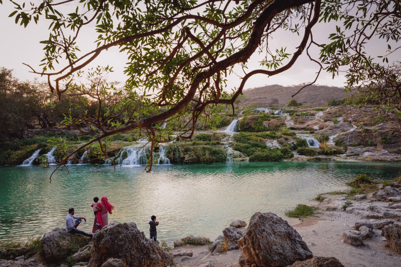 A family stands in front of waterfalls feeding into a watering hole.