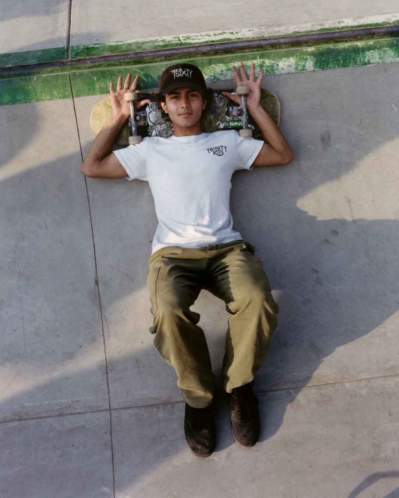A Pakistani skateboarder lays down with their head resting on their skateboard.