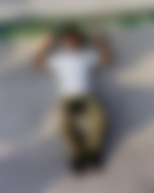 A Pakistani skateboarder lays down with their head resting on their skateboard.