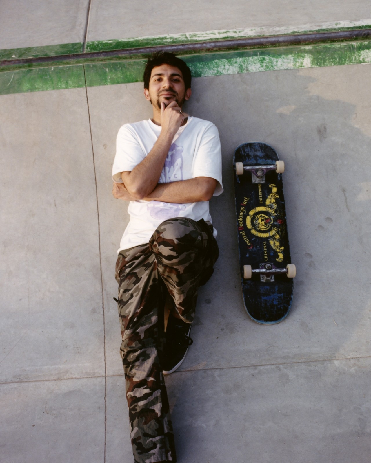 A Pakistani skater lays down in a skatepark next to their skateboard.